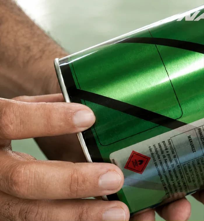 Mano sosteniendo una lata de Pegamento Amazonas por el cuerpo, con la etiqueta y los pictogramas de seguridad a la vista.
